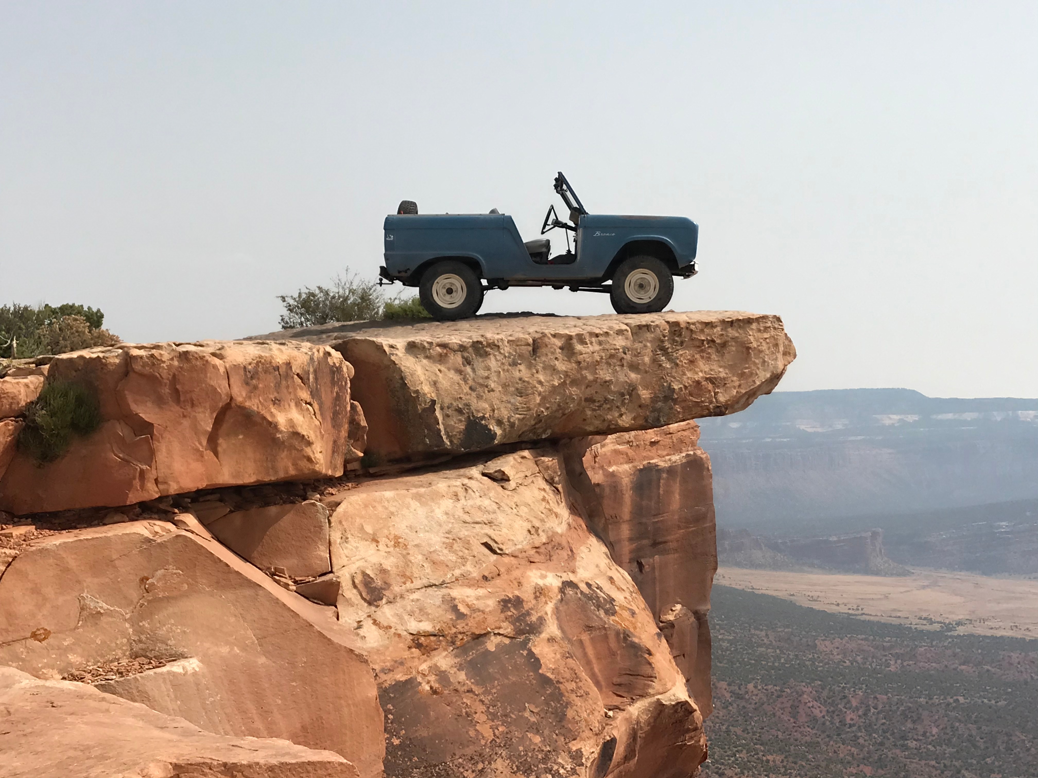 A vintage Bronco truck parked on the edge of a cliff